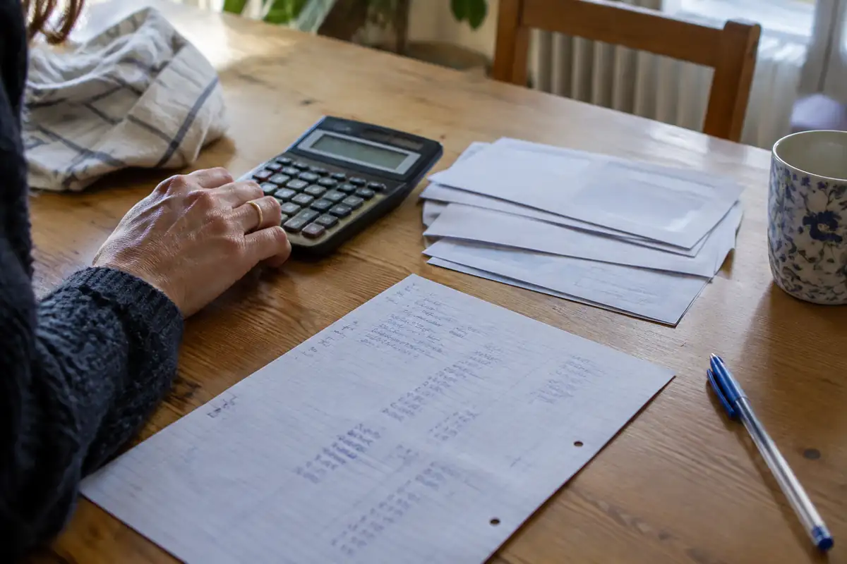 Calculatrice, enveloppes et feuille de calculs manuscrits sur une table en bois